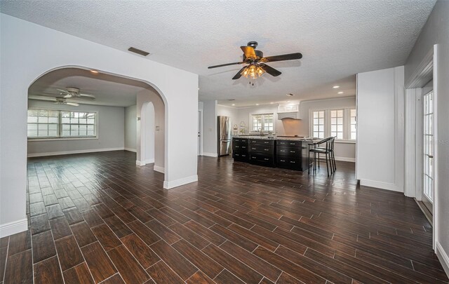 1402 Oleander Dr, Tarpon Springs, FL 34689 - unfurnished living room with a ceiling fan, arched walkways, baseboards, dark wood-type flooring, and a textured ceiling