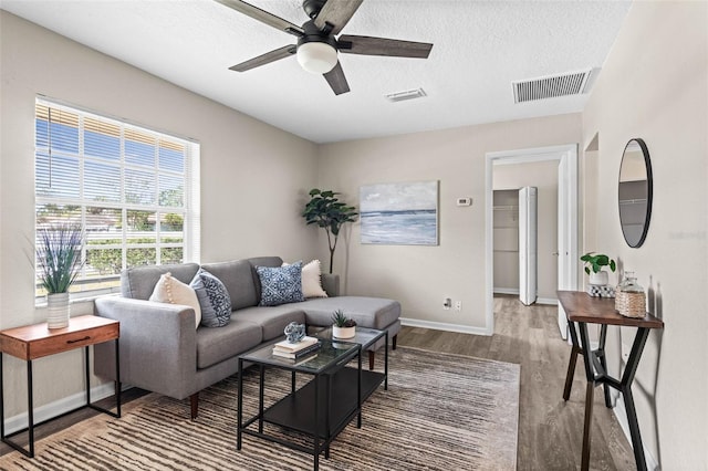 living area with a ceiling fan, wood finished floors, baseboards, and a textured ceiling