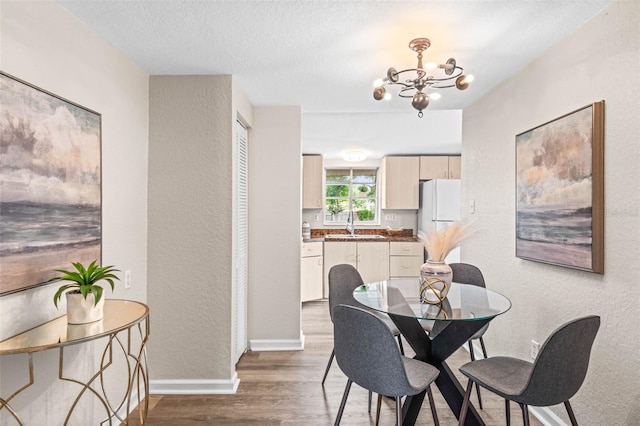 dining area with a textured wall, wood finished floors, a chandelier, baseboards, and a textured ceiling