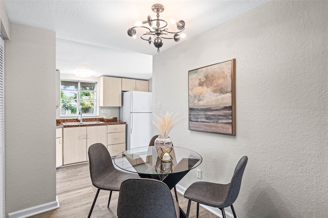 dining space featuring a textured wall, a chandelier, light wood-style floors, and baseboards