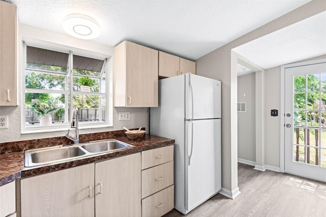 kitchen with a sink, light brown cabinets, freestanding refrigerator, light wood-style floors, and dark countertops