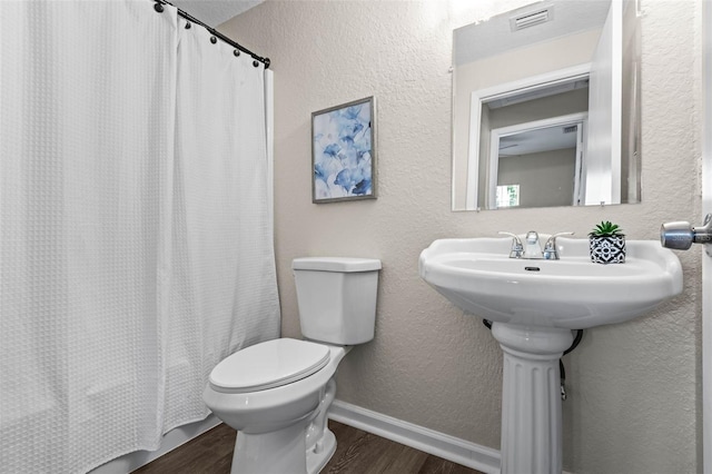 bathroom with wood finished floors, toilet, baseboards, and a textured wall