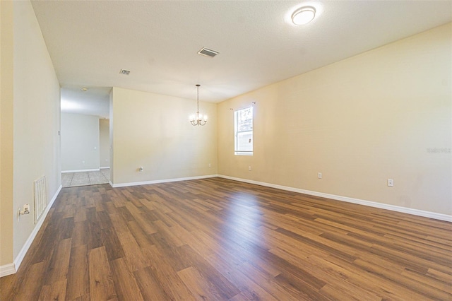 unfurnished room with a chandelier, dark wood-style flooring, and baseboards