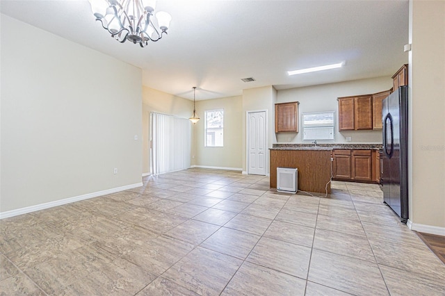 kitchen featuring freestanding refrigerator, a kitchen island, a chandelier, brown cabinets, and open floor plan