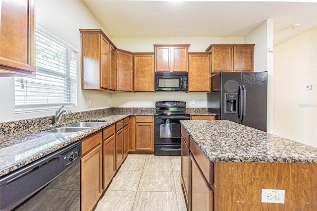 kitchen featuring black appliances, a sink, brown cabinets, dark stone counters, and a center island