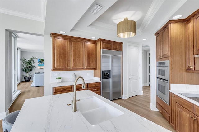 140 Riviera Dunes Way Unit 1203, Palmetto, FL 34221 - kitchen with stainless steel appliances, a sink, crown molding, light wood-type flooring, and brown cabinets