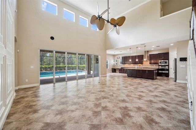 5117 Longspur Ct, Lithia, FL 33547 - unfurnished living room featuring a ceiling fan, crown molding, a high ceiling, plenty of natural light, and baseboards