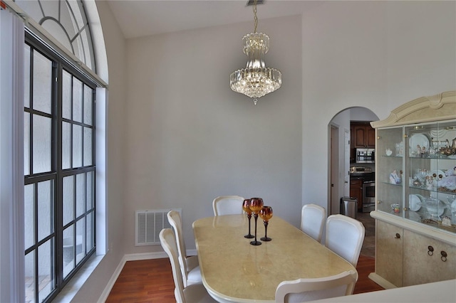 dining space with arched walkways, a chandelier, dark wood-style floors, baseboards, and a towering ceiling