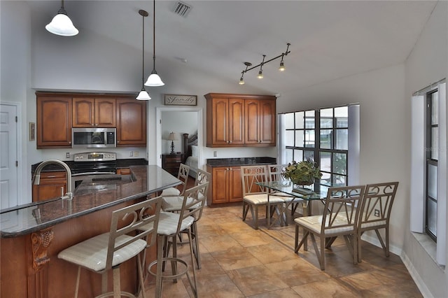 kitchen with appliances with stainless steel finishes, a breakfast bar, dark stone counters, pendant lighting, and brown cabinets