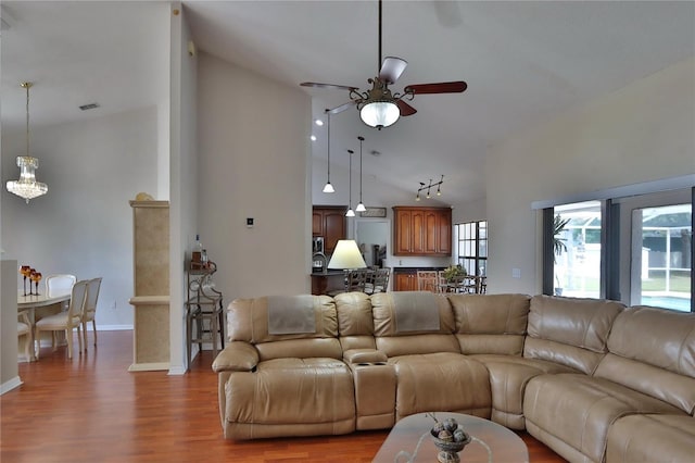 living area featuring a ceiling fan, wood finished floors, high vaulted ceiling, baseboards, and a chandelier