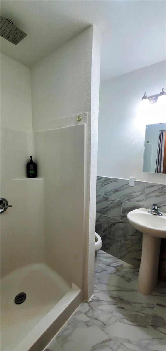 8207 Volusia Pl, Tampa, FL 33637 - bathroom with a stall shower, toilet, tile walls, and a wainscoted wall