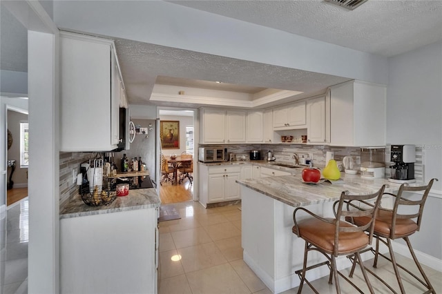 2219 Summit View Dr, Valrico, FL 33596 - kitchen with a peninsula, tasteful backsplash, a sink, white cabinetry, and a textured ceiling