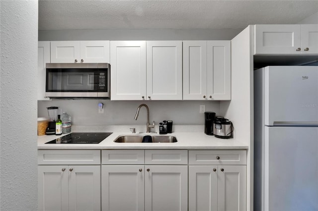 2219 Summit View Dr, Valrico, FL 33596 - kitchen featuring freestanding refrigerator, stainless steel microwave, a sink, black electric cooktop, and white cabinetry