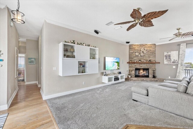 living area with a ceiling fan, ornamental molding, light wood-type flooring, a stone fireplace, and baseboards