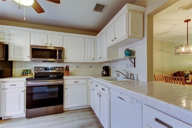 2913 Fig Ct, Palm Harbor, FL 34684 - kitchen featuring appliances with stainless steel finishes, a sink, tile countertops, white cabinetry, and ceiling fan