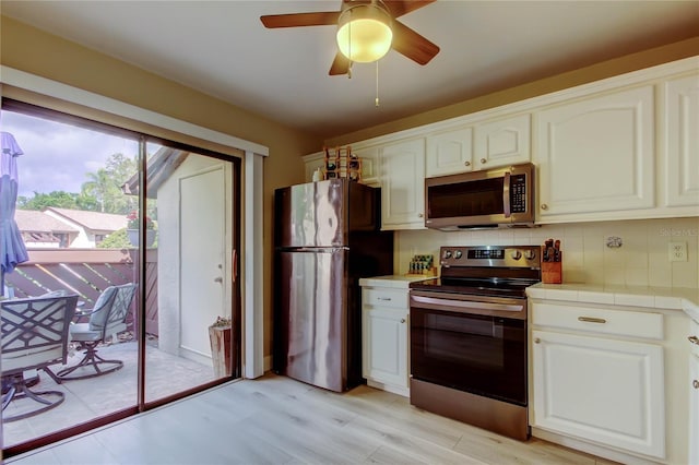 2913 Fig Ct, Palm Harbor, FL 34684 - kitchen featuring appliances with stainless steel finishes, tile counters, a ceiling fan, backsplash, and white cabinetry