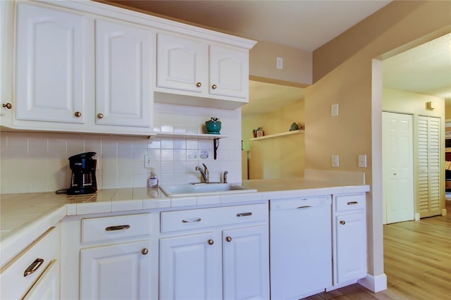 2913 Fig Ct, Palm Harbor, FL 34684 - kitchen featuring white dishwasher, a sink, decorative backsplash, white cabinetry, and light wood finished floors
