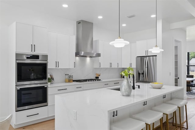 kitchen featuring wall chimney exhaust hood, appliances with stainless steel finishes, a breakfast bar area, a sink, and a center island with sink