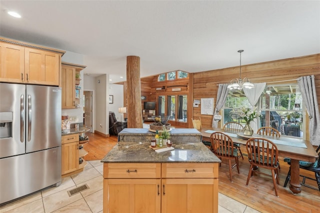 5817 Myrtle Ln, Tampa, FL 33625 - kitchen featuring stainless steel refrigerator with ice dispenser, wood walls, dark stone countertops, a kitchen island, and decorative light fixtures