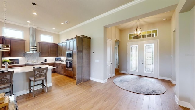 426 Bourganville Dr, Palm Coast, FL 32137 - kitchen with wall chimney exhaust hood, light countertops, french doors, hanging light fixtures, and a kitchen bar