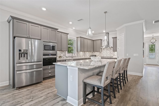 4166 Epic Cv, Land O Lakes, FL 34638 - kitchen featuring stainless steel appliances, wall chimney exhaust hood, gray cabinetry, a kitchen island, and light wood-style floors