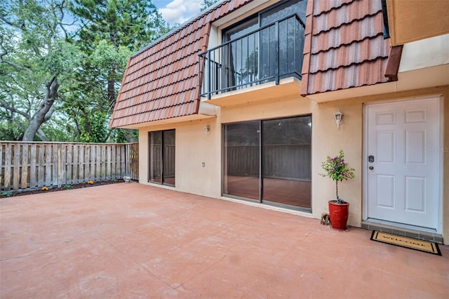 back of property with a tile roof, a balcony, stucco siding, and fence