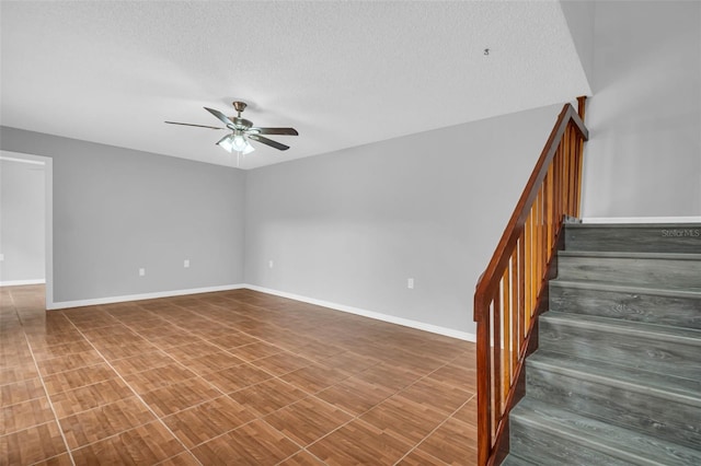 stairs with ceiling fan, a textured ceiling, and baseboards