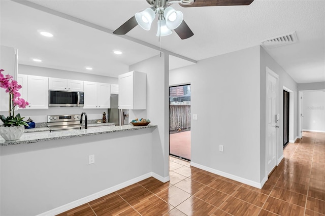 kitchen with stainless steel appliances, ceiling fan, white cabinetry, light stone countertops, and baseboards