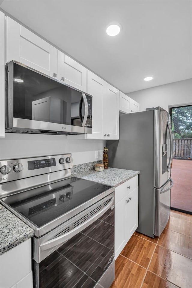 kitchen with appliances with stainless steel finishes, white cabinets, light wood finished floors, light stone counters, and recessed lighting