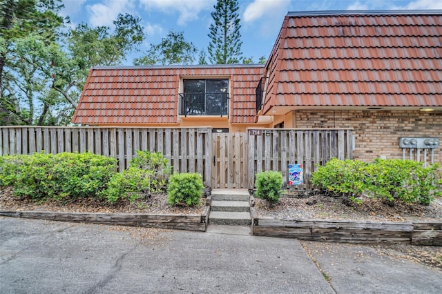 property entrance with a tile roof, fence, brick siding, and mansard roof