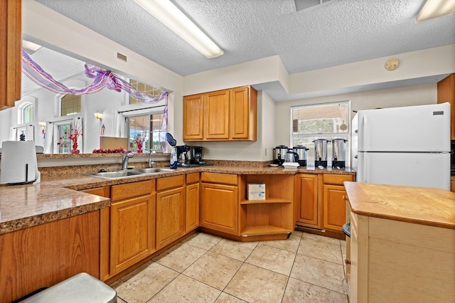 kitchen featuring a sink, freestanding refrigerator, a textured ceiling, light tile patterned floors, and brown cabinets