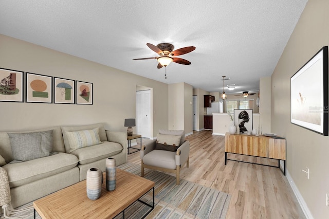 living area featuring ceiling fan, light wood-style flooring, baseboards, and a textured ceiling