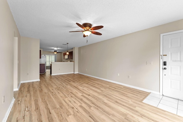 unfurnished living room featuring ceiling fan, light wood-style flooring, a textured ceiling, and baseboards