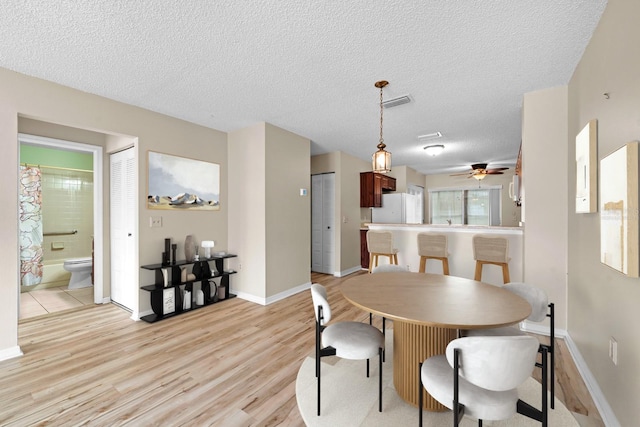 dining space featuring light wood-type flooring, a textured ceiling, a ceiling fan, and baseboards