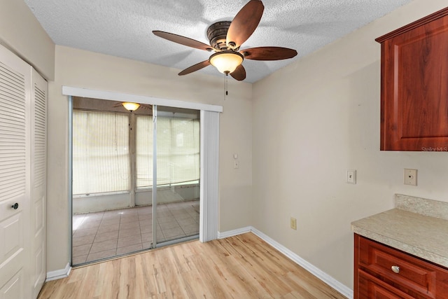 unfurnished dining area featuring a ceiling fan, light wood-type flooring, a textured ceiling, and baseboards