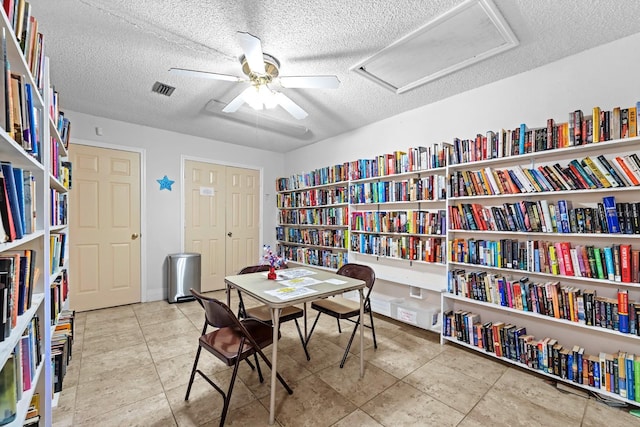 sitting room with attic access, a ceiling fan, a textured ceiling, bookshelves, and tile patterned flooring
