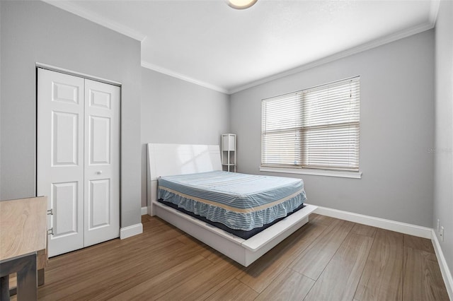 bedroom featuring a closet, baseboards, wood finished floors, and ornamental molding