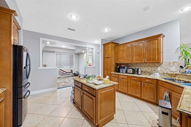 kitchen with stainless steel fridge, a sink, brown cabinetry, light tile patterned floors, and a textured ceiling