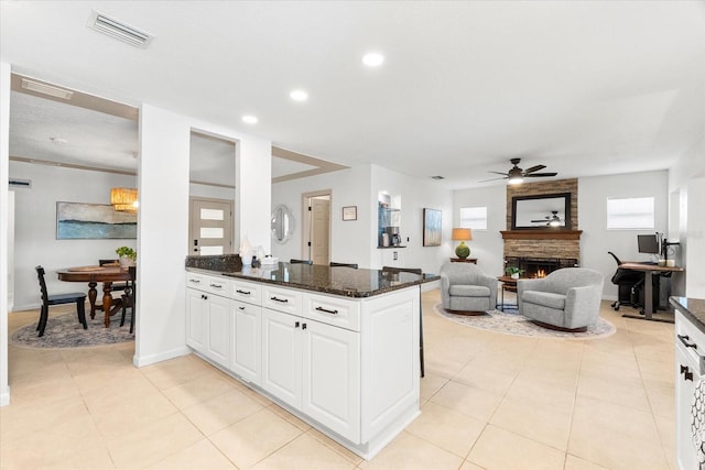 8848 Sunlit Cove Dr NE, Saint Petersburg, FL 33702 - kitchen featuring ceiling fan, a stone fireplace, white cabinets, dark stone counters, and a peninsula