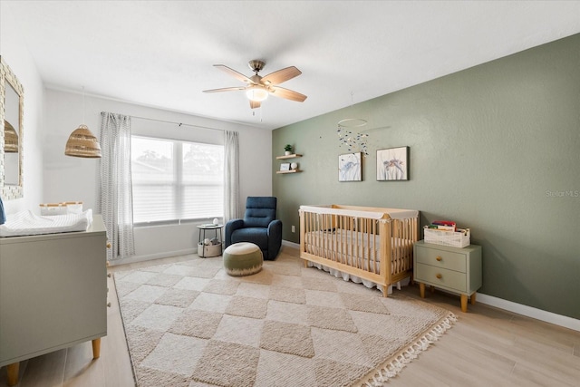 8848 Sunlit Cove Dr NE, Saint Petersburg, FL 33702 - bedroom featuring a crib, baseboards, light wood-type flooring, and a ceiling fan