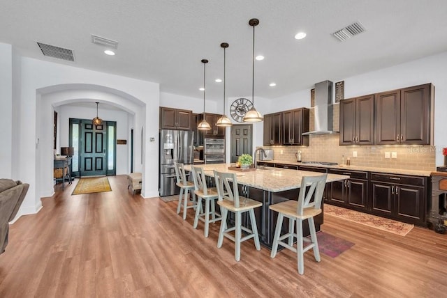kitchen with wall chimney range hood, appliances with stainless steel finishes, arched walkways, light wood finished floors, and recessed lighting