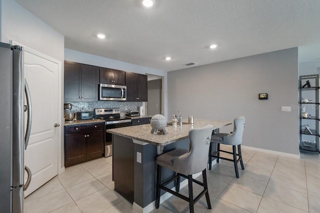 9532 Black Walnut Dr, Clermont, FL 34715 - kitchen featuring stainless steel appliances, a breakfast bar, light tile patterned floors, a center island with sink, and a textured ceiling
