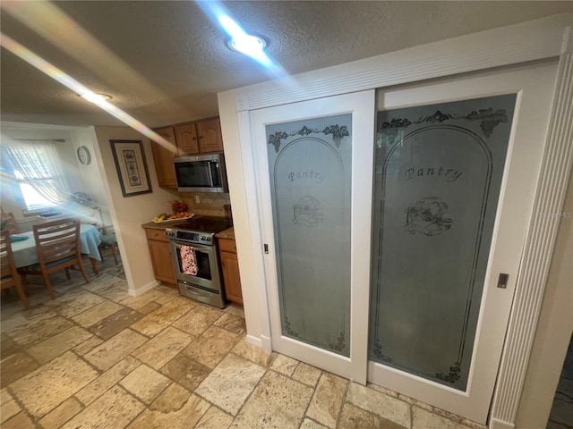 6073 115th Ave N, Pinellas Park, FL 33782 - kitchen featuring stainless steel appliances, a textured ceiling, stone tile flooring, tasteful backsplash, and brown cabinetry