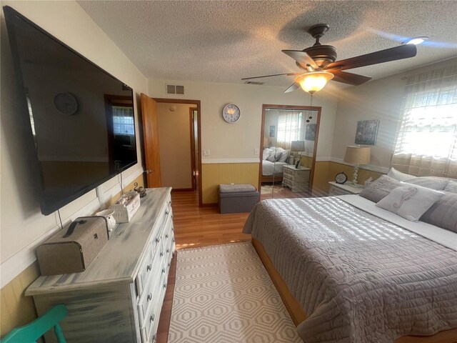 6073 115th Ave N, Pinellas Park, FL 33782 - bedroom featuring a wainscoted wall, light wood-style flooring, a textured ceiling, and a ceiling fan