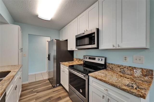 kitchen featuring stainless steel appliances, light wood finished floors, white cabinets, a textured ceiling, and light stone counters