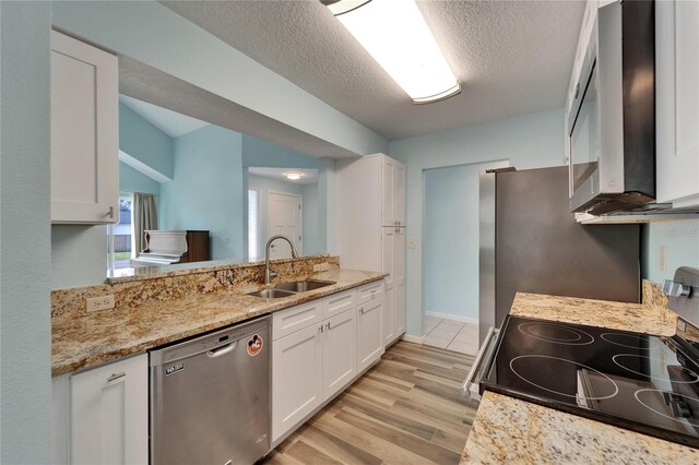 kitchen with appliances with stainless steel finishes, a sink, white cabinets, light wood-type flooring, and a textured ceiling