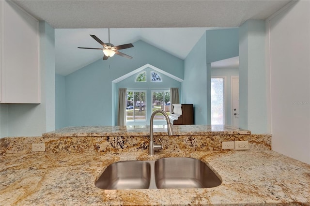 kitchen with a sink, light stone counters, ceiling fan, white cabinetry, and lofted ceiling
