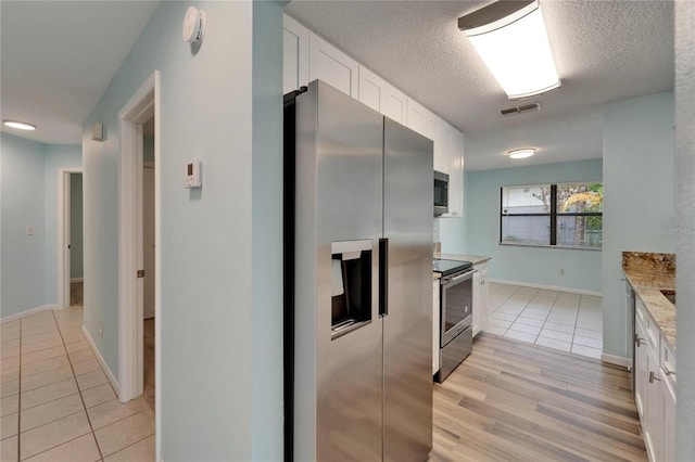 kitchen with stainless steel appliances, white cabinetry, light tile patterned flooring, baseboards, and a textured ceiling