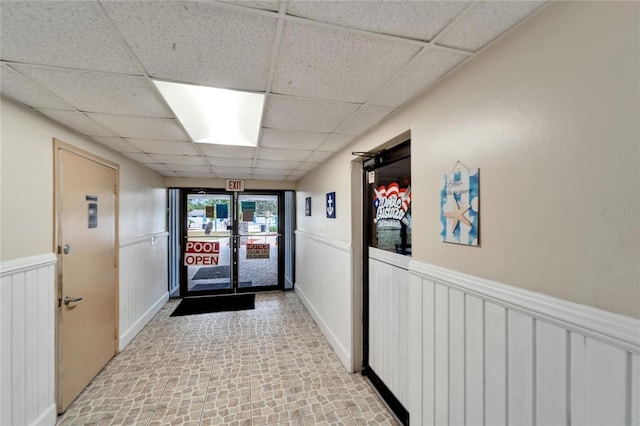 corridor featuring a paneled ceiling, wainscoting, and brick patterned floors