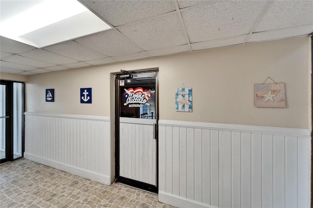 basement with a drop ceiling and a wainscoted wall